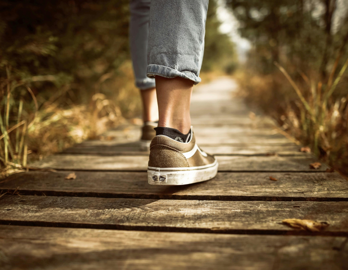 Close up on a persons legs while they walk down a wooden path in the woods Close up on a persons legs while they walk down a wooden path in the woods